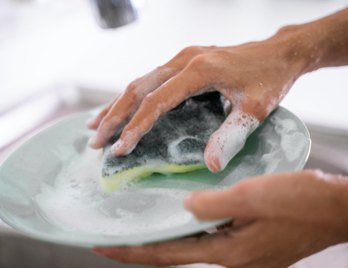 Une personne lave une assiette avec une éponge.
