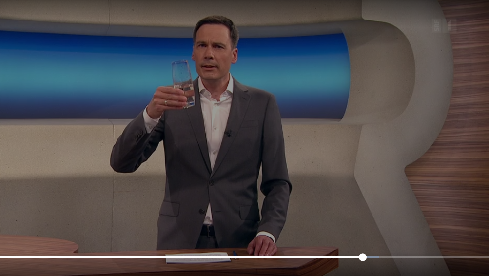 Ein Mann im Anzug hält ein Glas Wasser in der Hand.