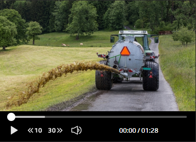 Ein Traktor fährt eine Landstraße entlang und schüttet Gülle aus.