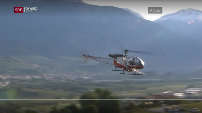 Ein Hubschrauber fliegt in einem Tal mit Bergen im Hintergrund.