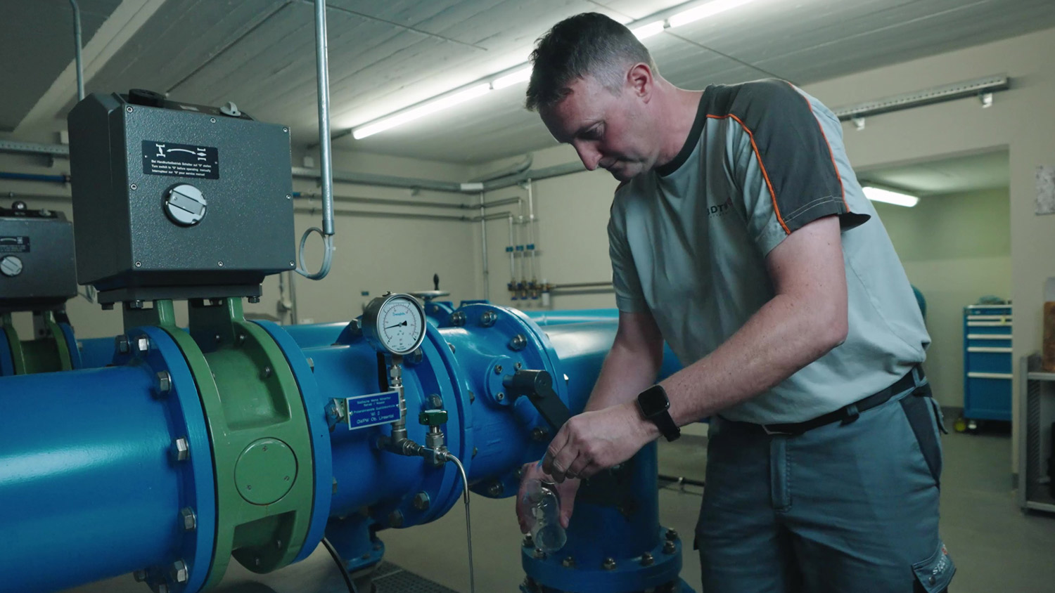 Ein Brunnenmeister, der an einer blauen Wasserpumpe arbeitet.
