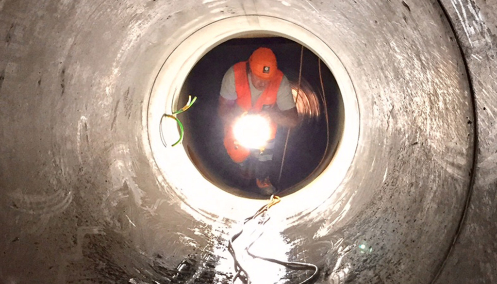 Ein Entwässerungstechnologe arbeitet in einem dunklen Rohr mit einem Licht in der Hand.