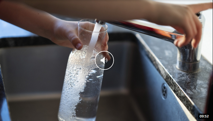 Eine Person gießt Wasser aus einem Glas in ein Waschbecken.
