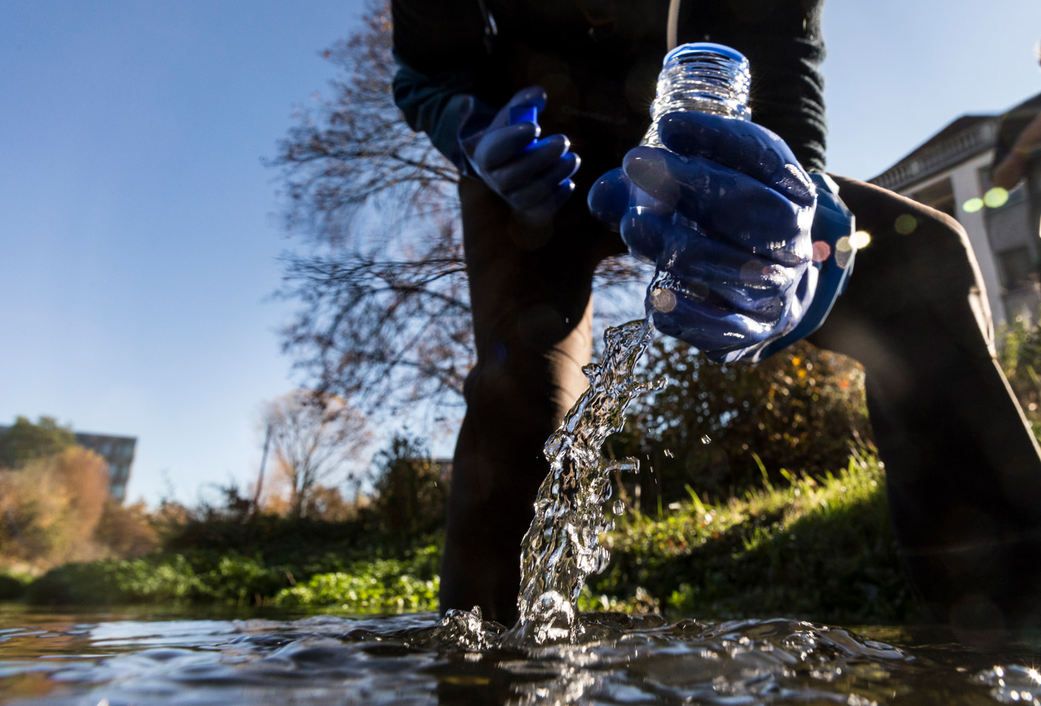 Une personne verse de l'eau d'une bouteille dans un ruisseau.