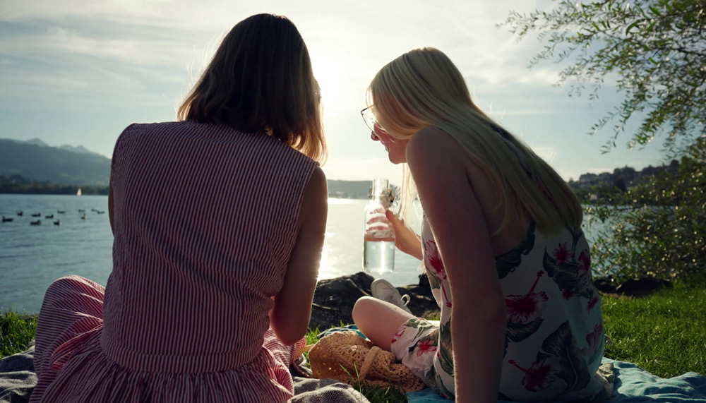 Zwei Mädchen sitzen im Gras neben einem See.