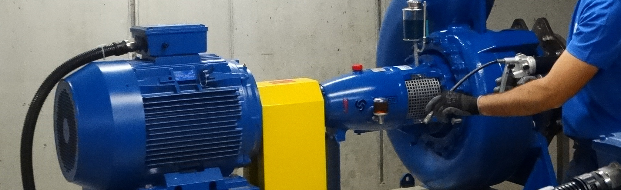 Eine blau gekleidete Person bedient eine große blau-gelbe Industrie-Kreiselpumpenanlage in einem Gebäude.