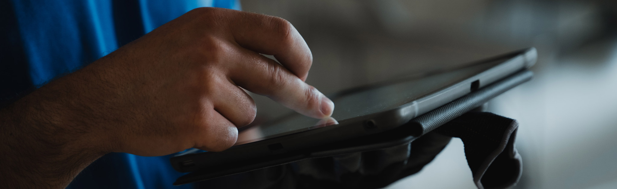 Eine Person benutzt ihren Finger, um mit einem Touchscreen-Tablet-Gerät zu interagieren, indem sie es in einer Hand hält und mit der anderen Hand auf den Bildschirm tippt.