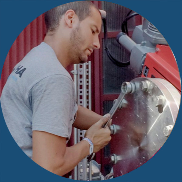 Ein Mann in einem grauen T-Shirt zieht mit einem Schraubenschl&uuml;ssel Schrauben an Industriemaschinen fest.